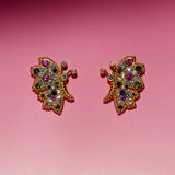 Butterfly Bloom stud earrings featuring pink and blue sapphires, white diamonds and green tsavorite, photographed against a pink background