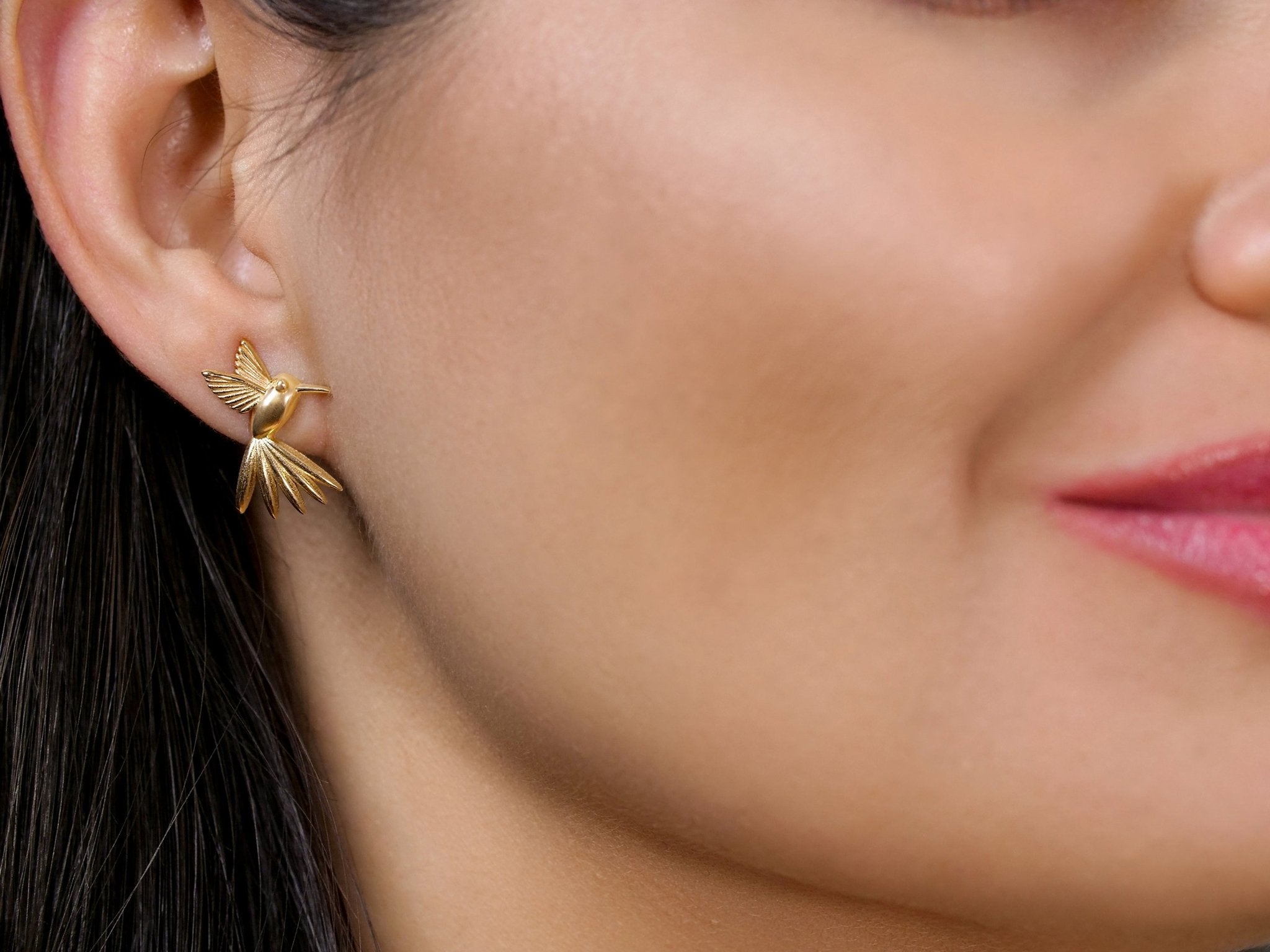 Golden Hummingbird stud earrings in solid gold worn on a model’s ear from the Humming Beauty collection by Aurora Laffite Jewelry.